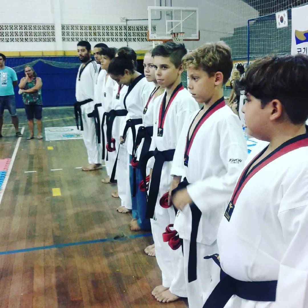 Fila de examinandos de Taekwondo de dobok branco, perfilados no ginásio durante o exame de faixa